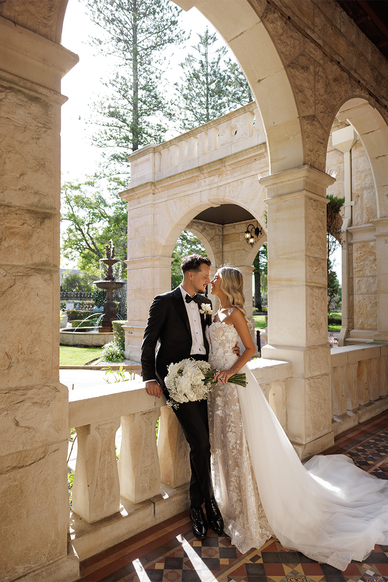 Bride and groom about to kiss under a stone archway in an outdoors patio.